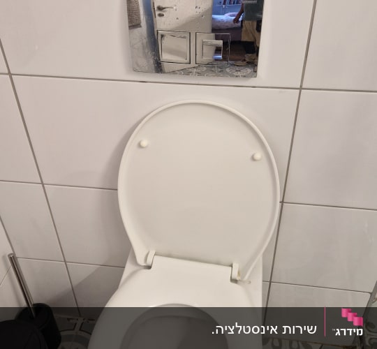 אסלה לבנה עם לחצן הדחה על קיר אריחים